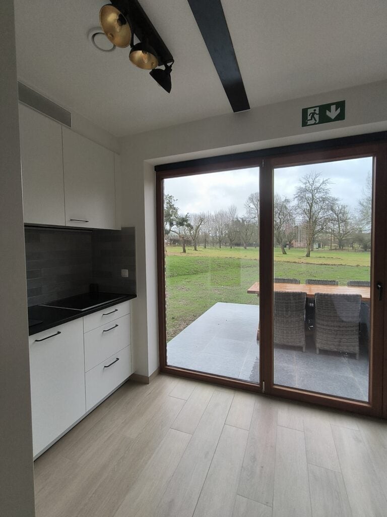 Uitzicht op het terras en de hoogstamboomgaard vanuit de keuken van het brouwhuis van de vakantiewoning bij Hof van Sassenbroek in Tongeren‑Borgloon, Haspengouw.